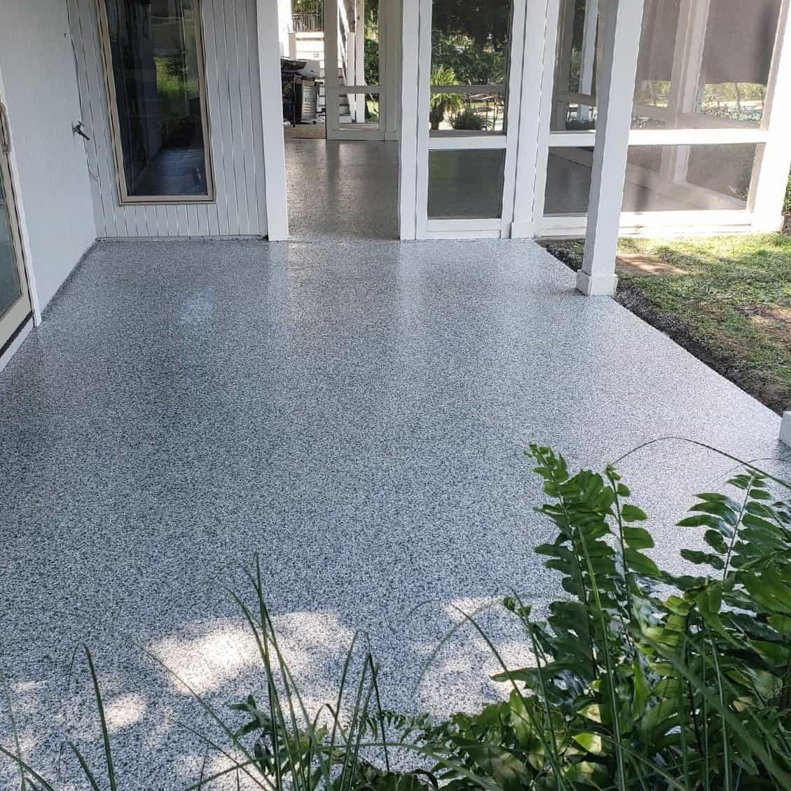 Gray coated patio floor beside screened doors and a garden